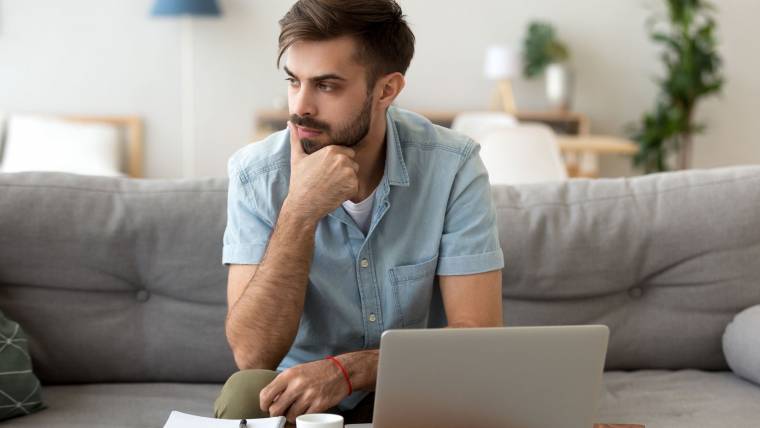 man sitting on a couch with his laptop, papers, and coffee in front of him