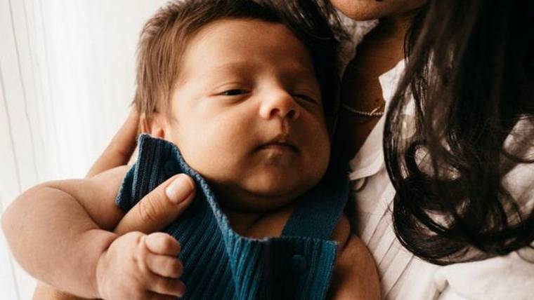 A mother smiles at the newborn baby in her arms