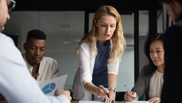 A woman stands over a conference table talking to colleagues