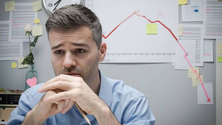 a man frowns and looks away as a downward-trending graph looms behind him