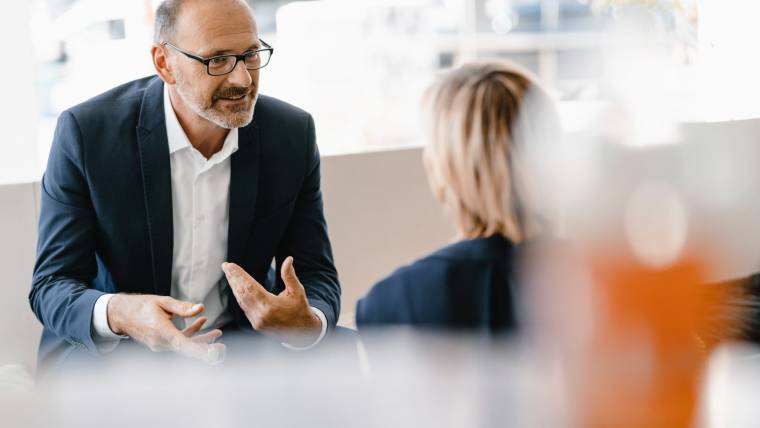 A man tin glasses talks to a colleague