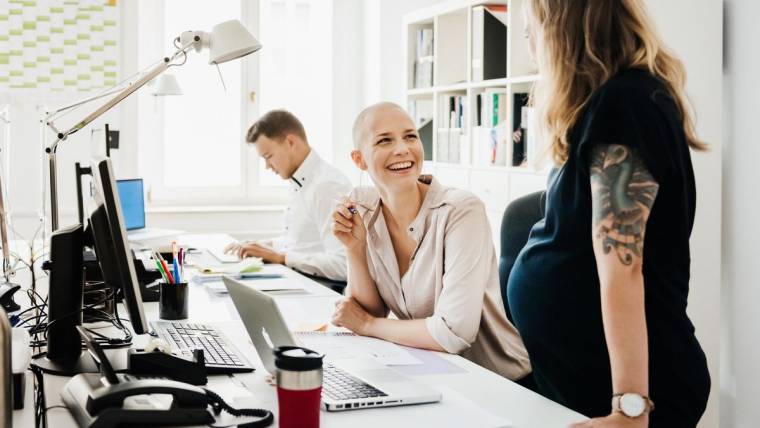 A pregnant woman talks with a colleague