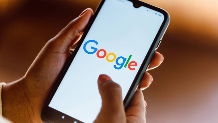 Hands holding a mobile device showing the Google logo