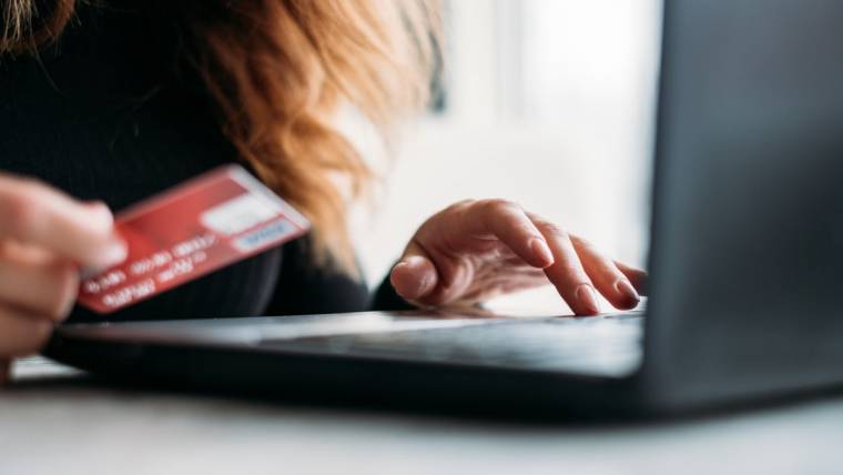 A woman holds a credit card while typing on a computer