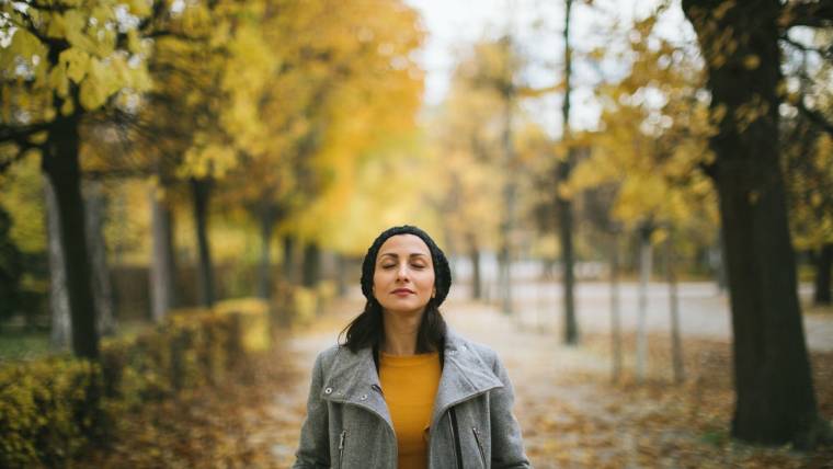 A woman closes her eyes as she stands outside in crisp fall weather