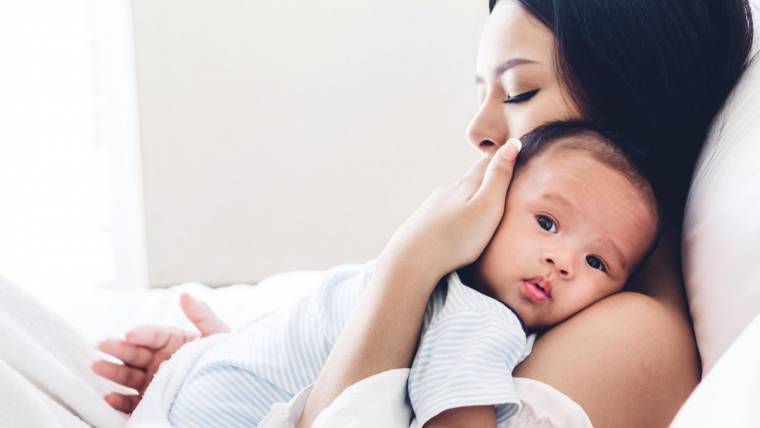 Woman lying in bed while holding her newborn baby