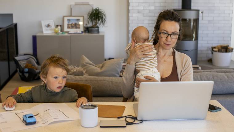 woman holding an infant sitting at a computer next to toddler