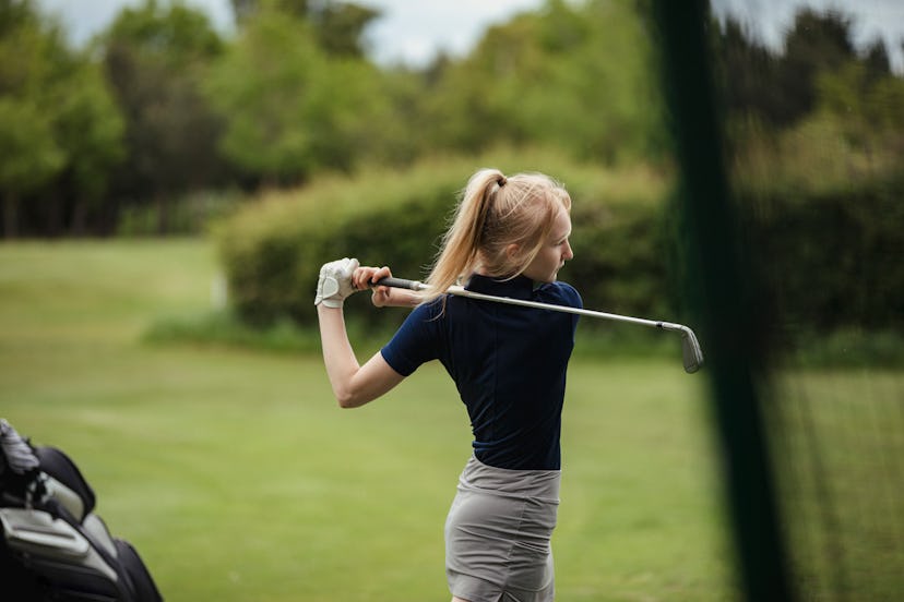 A side view shot of a teenage girl swinging her club at the golf course, in a story about sports kid...