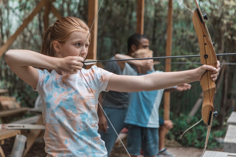 Two children take aim with their bows and arrows at an archery range, in a story about sports kids c...