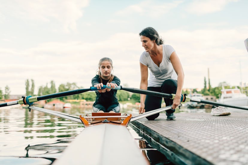 Teen girl in a crew boat while her coach speaks to her from the dock, in a story about sports kids c...