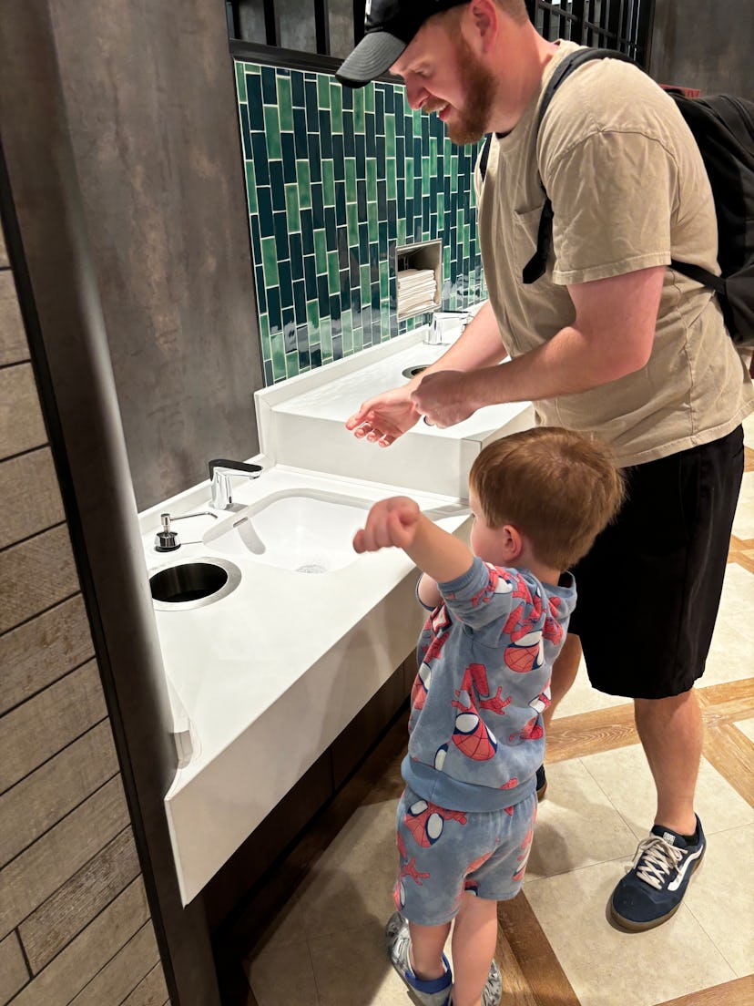 A toddler boy pushed up his sleeves as his dad helps him wash his hands on board the Disney Treasure...