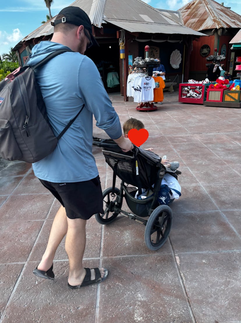 A dad pushes his son in a stroller past a gift shop on Disney's Castaway Cay