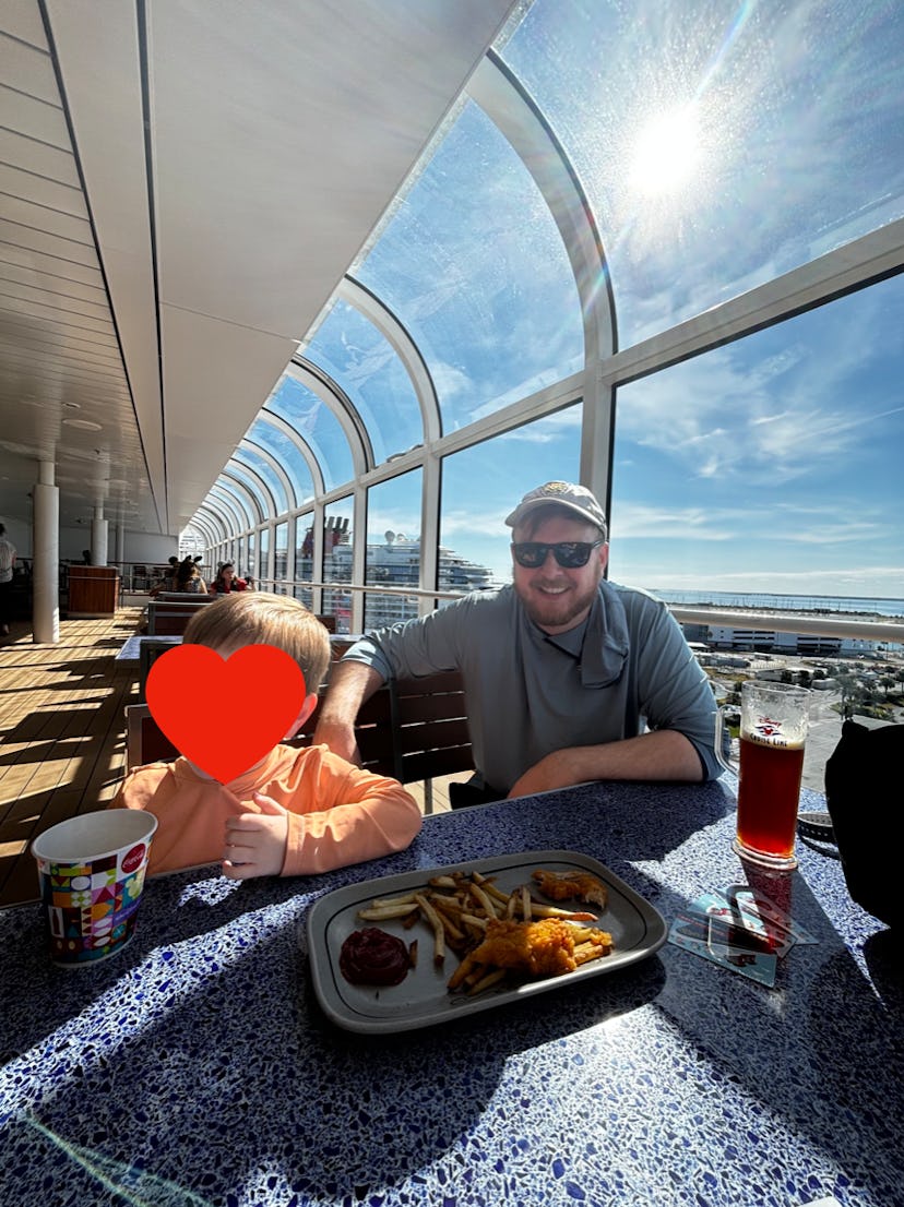 A dad and child enjoy chicken tenders and fries on board the Disney Treasure